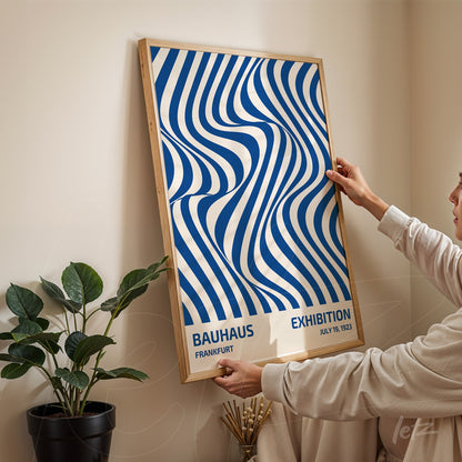 poster featuring abstract blue and white wavy lines art in a light wood frame being held by a person
