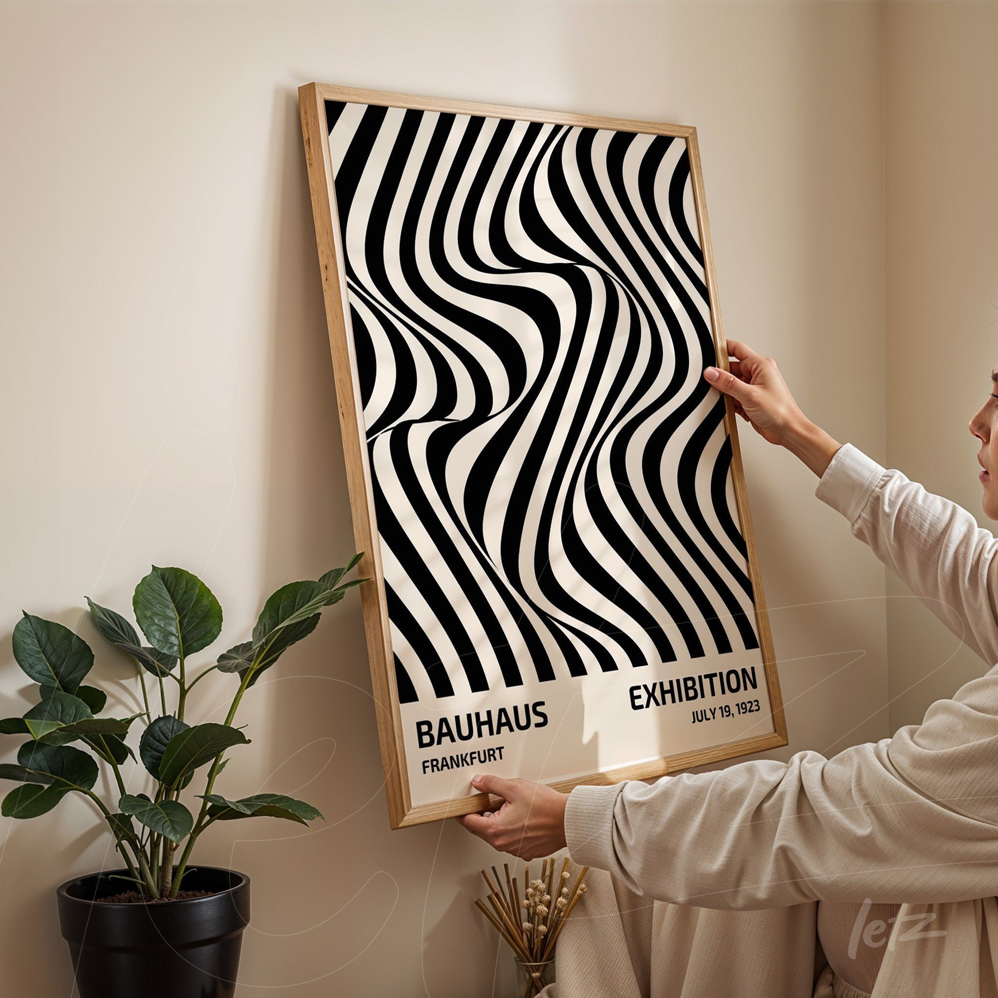poster with black and white wavy line abstract pattern, framed in light wood, held by a person against a cream-colored wall