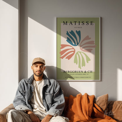 modern art print featuring soft colored leaf illustrations in a thin frame, displayed beside a young man sitting on a sofa with an orange blanket