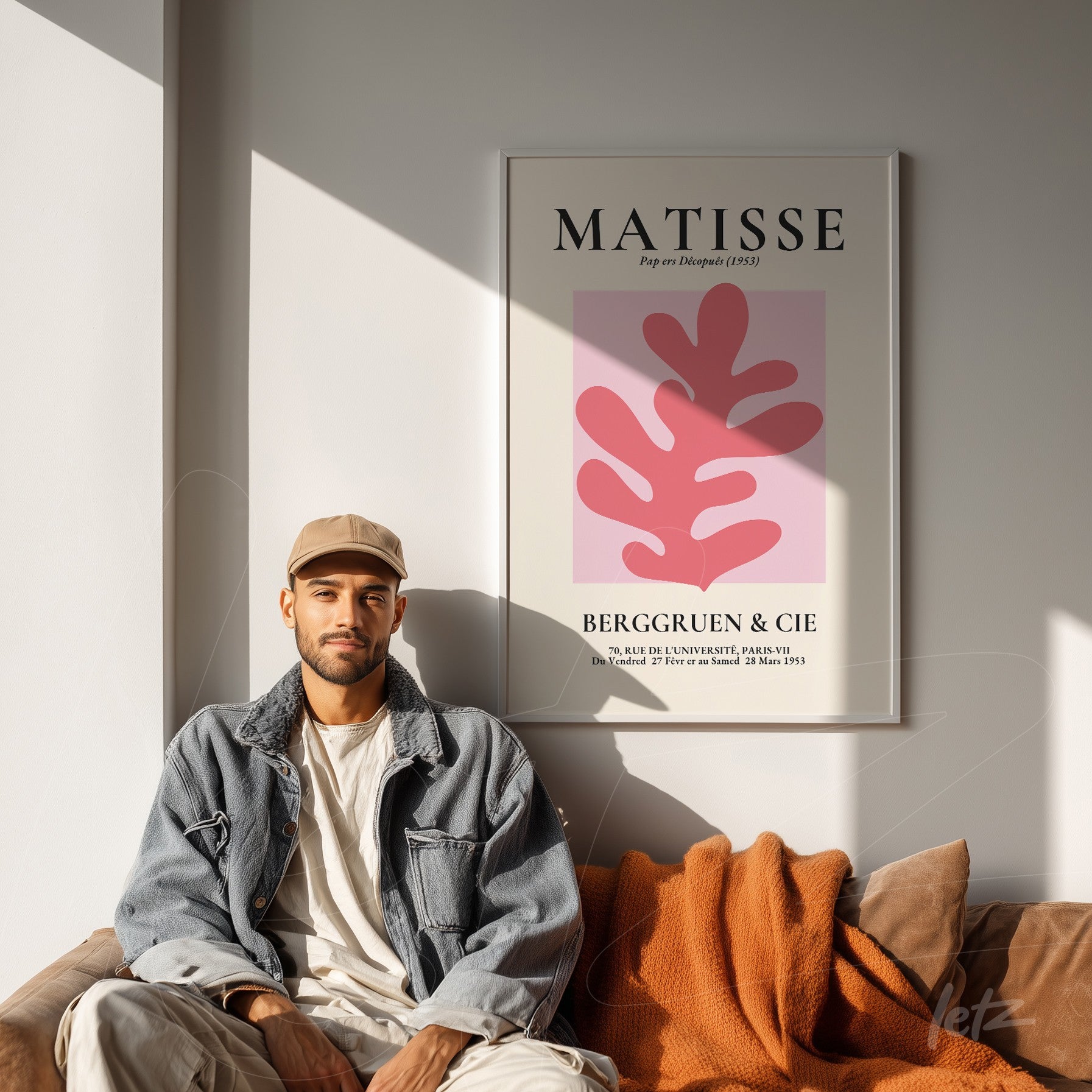 framed modern art piece featuring pink background and red leaves, displayed on a well-lit wall with a brown sofa and orange throw blanket