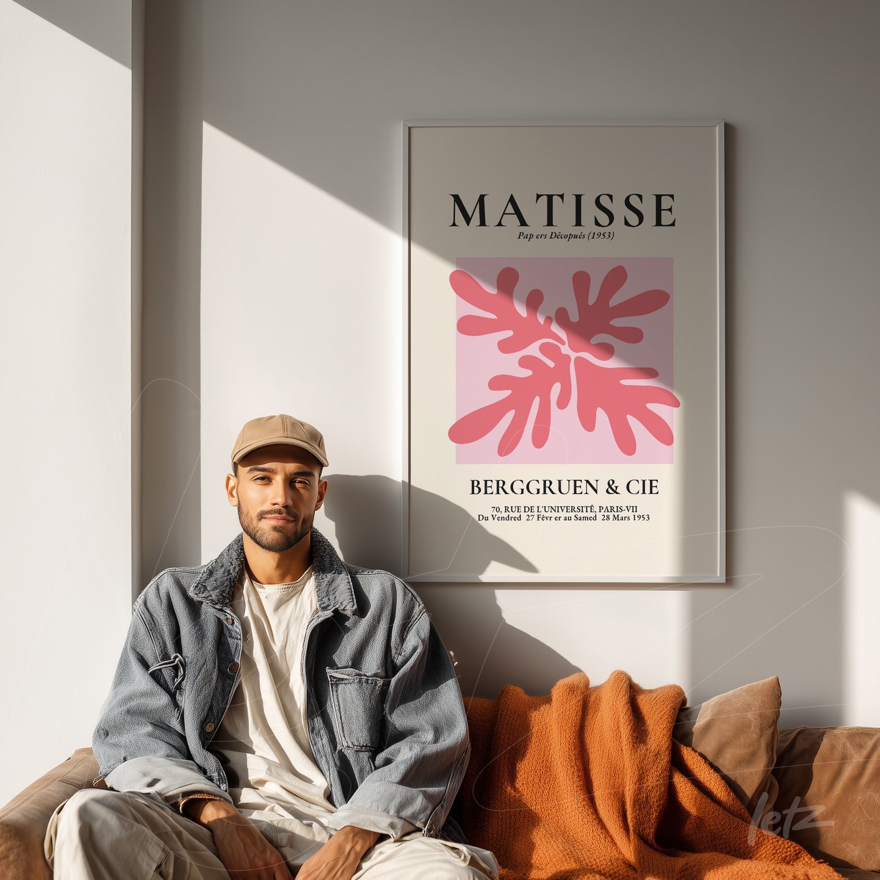 framed wall art featuring modern Matisse design with pink leaves displayed above a sofa with an orange blanket and a person sitting nearby