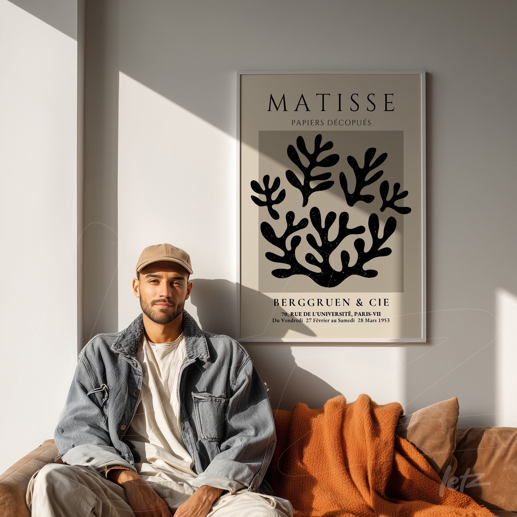 large framed artwork featuring abstract black leaves on light background displayed on a light wall beside a man sitting on a sofa