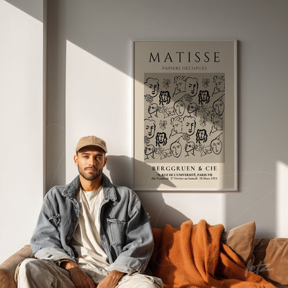 framed modern art piece by Matisse featuring black and white faces, displayed on a light wall beside a casually dressed man