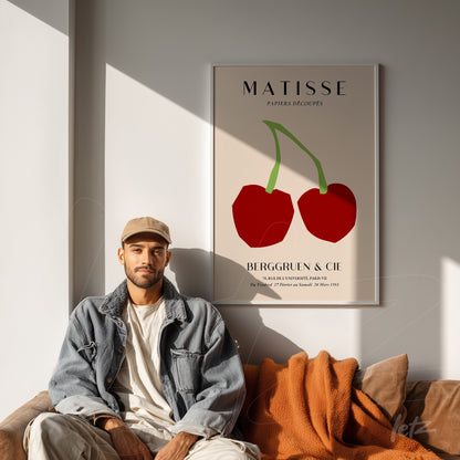 modern style wall art featuring red cherries on a cream background, framed and displayed on a light wall beside a man sitting on a couch