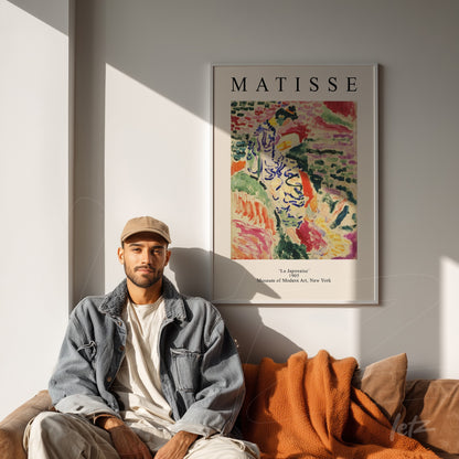 mockup featuring a framed modern art piece by Matisse displayed beside a man on a sofa with orange cushions