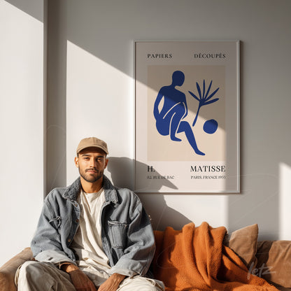 framed modern artwork of a blue human figure on light background, white frame prominently displayed in a room with brown sofa