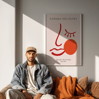 framed modern wall art by Henri Matisse featuring a minimalist face design in warm tones displayed on a white wall with a person sitting on a couch