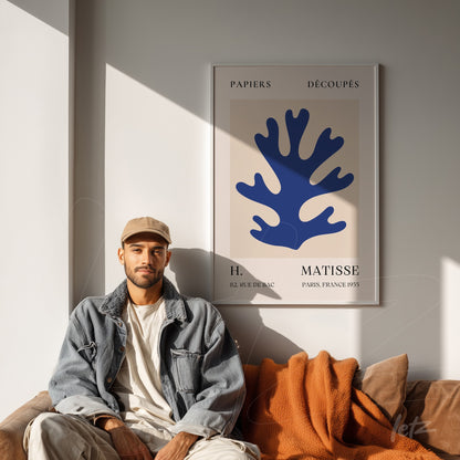 framed modern art piece featuring a blue coral shape against a nude background, displayed in a stylish setting with a brown leather sofa