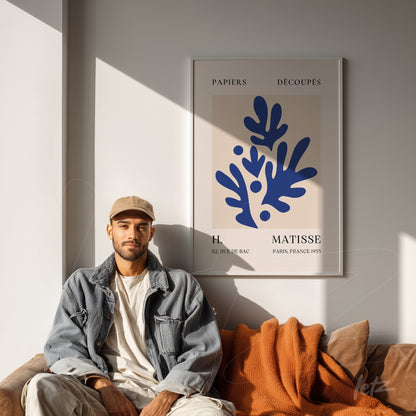 modernist wall art featuring organic shapes in blue, light frame displayed on a neutral wall beside a man sitting on a sofa