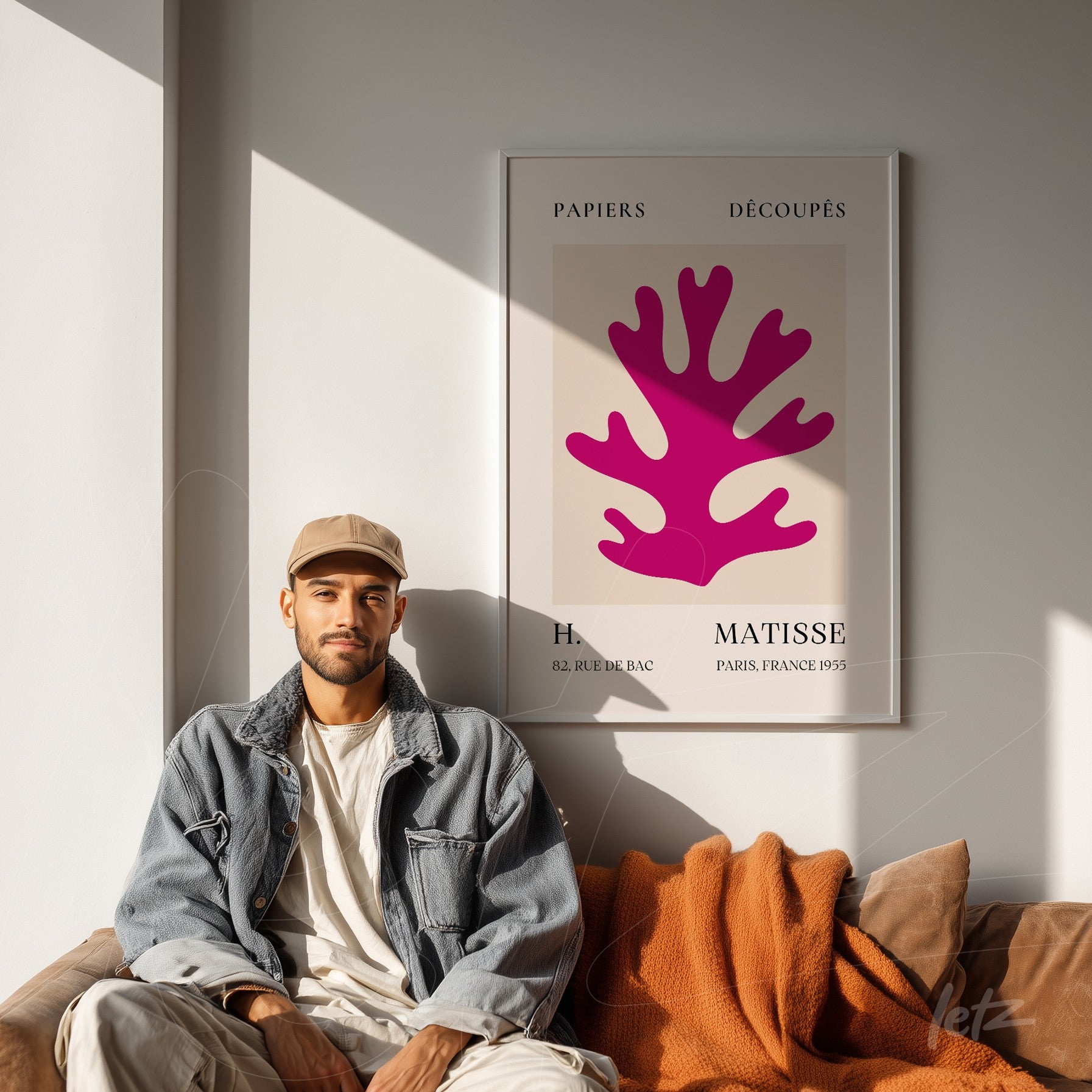 framed artwork featuring a pink coral design on light background displayed in a bright room, with a young man sitting on a sofa with orange pillows