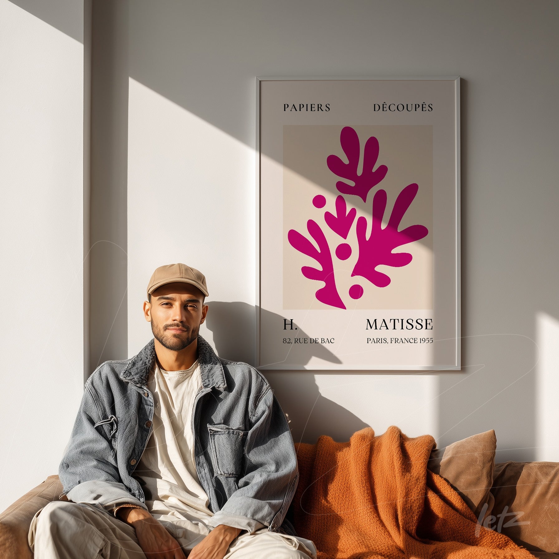 framed modern art print featuring stylized leaves in pink tones on a cream background, displayed on a well-lit wall with a person seated next to it