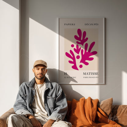 framed modern art print featuring stylized leaves in pink tones on a cream background, displayed on a well-lit wall with a person seated next to it