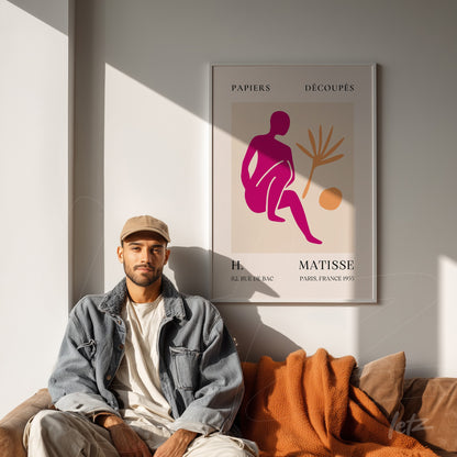 framed wall art featuring an abstract representation of a female figure in pink and orange tones displayed on a neutral wall beside a man sitting on a leather couch