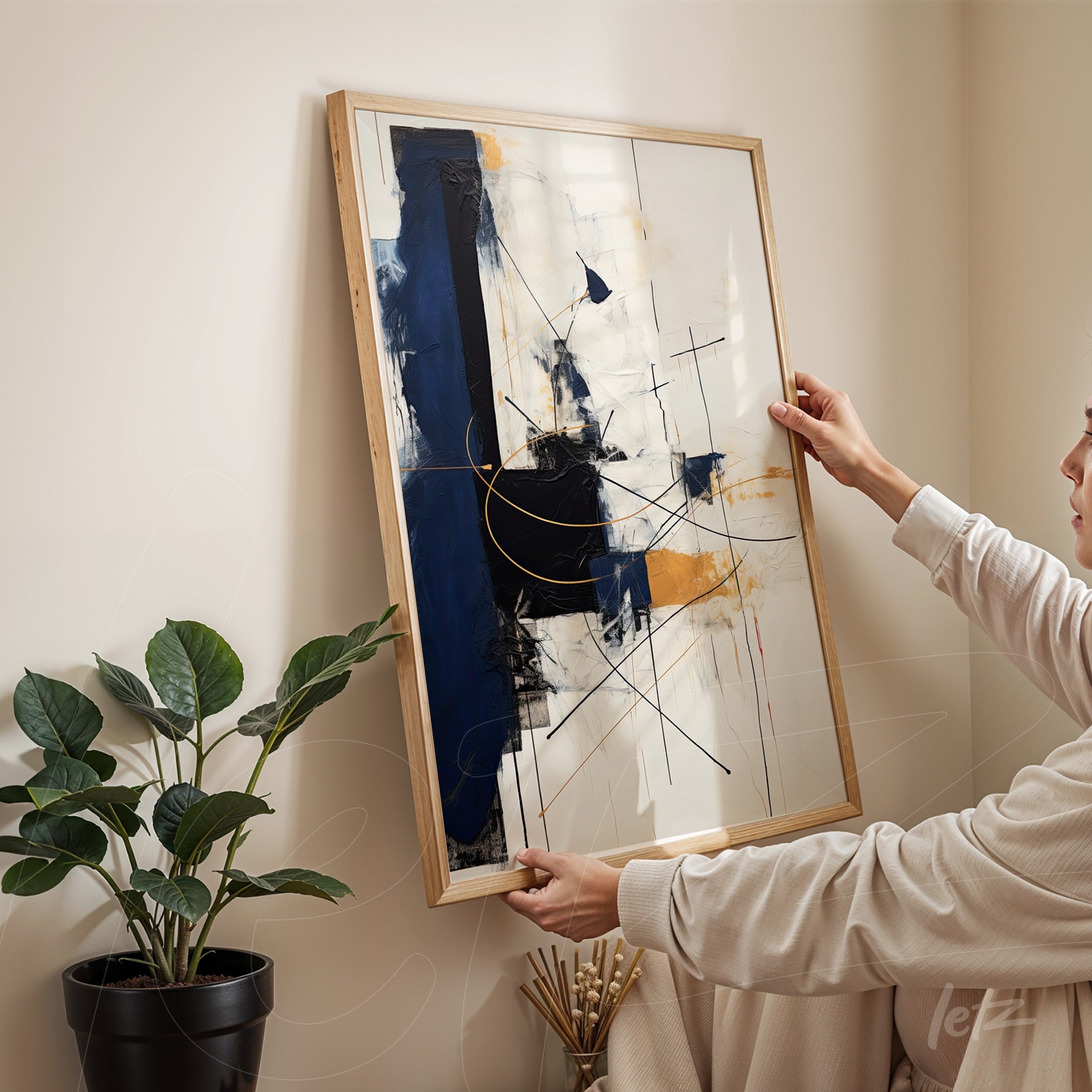 abstract artwork featuring geometric shapes in blue, gold, and white with a light wooden frame held by a woman in a cozy indoor setting