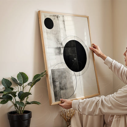 geometric wall art in black and white featuring circular shapes, held by a person in a bright setting with a plant in the background