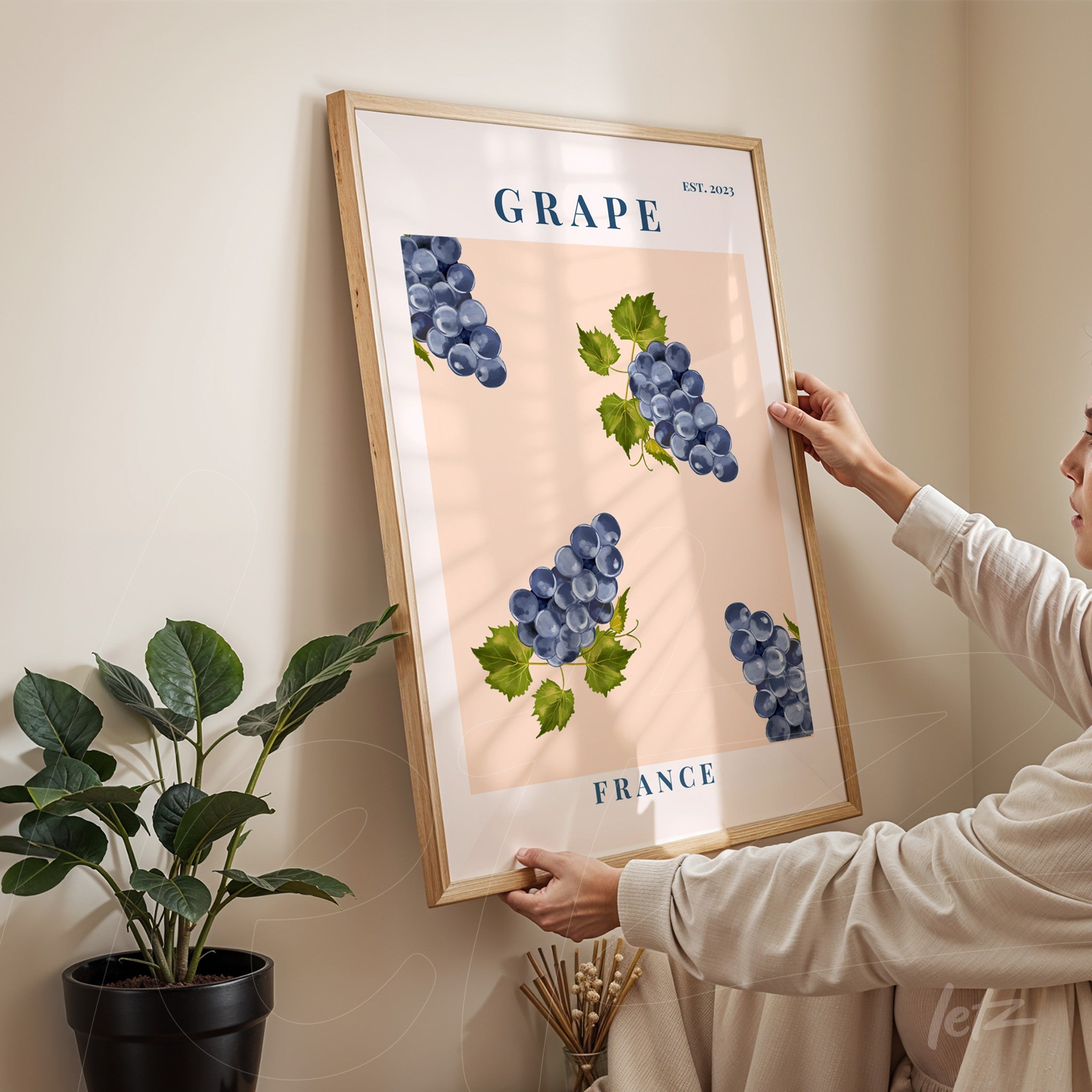 framed wall art featuring blue grape clusters on a pink background with light wood frame
