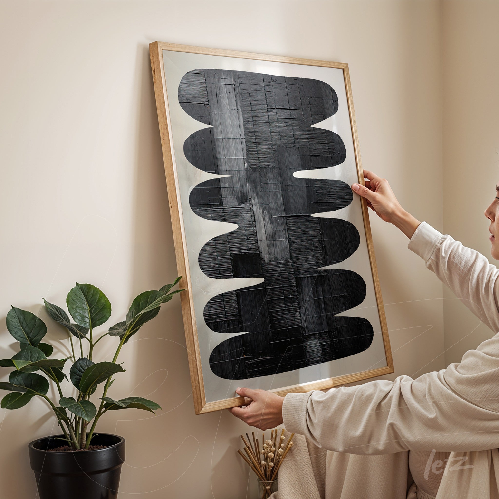 abstract wall art in light wood frame featuring black shapes on a light background, held by a person in a minimalist setting