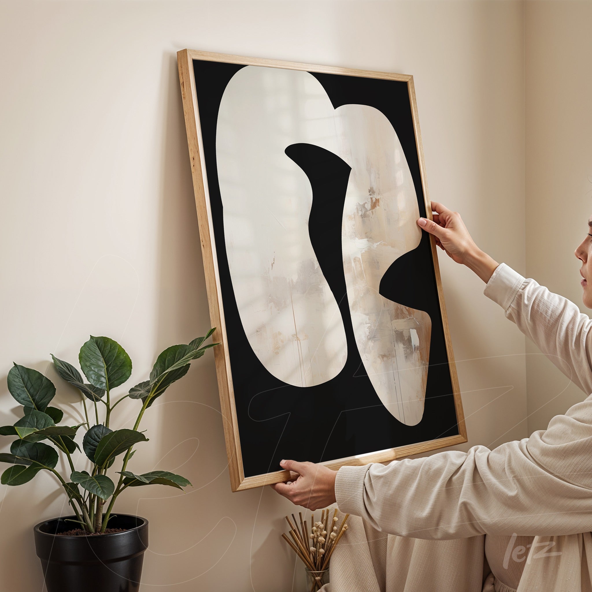 abstract artwork featuring organic shapes on black background held by a person in a light room with plant in the background