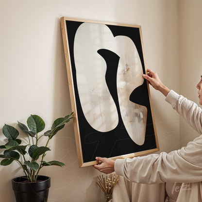 abstract artwork featuring organic shapes on black background held by a person in a light room with plant in the background