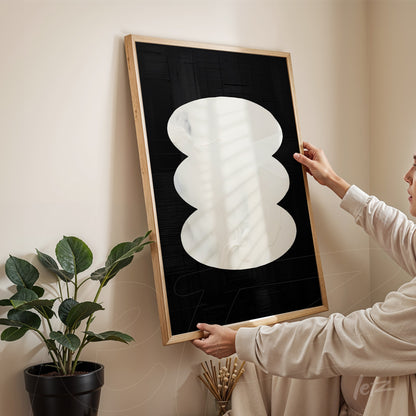 modern artwork featuring white organic shapes on a black background in a light wood frame held by a person