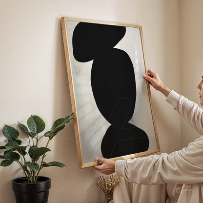 modern wall art featuring abstract black shapes on light background in light wood frame