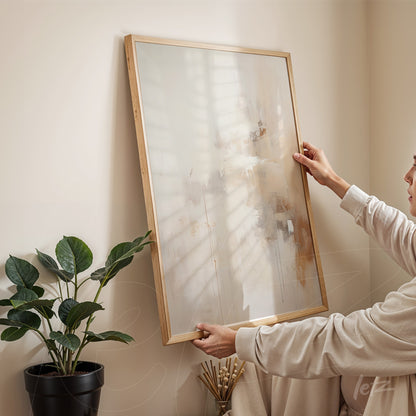 abstract wall art in light wood frame held by person in well-lit setting