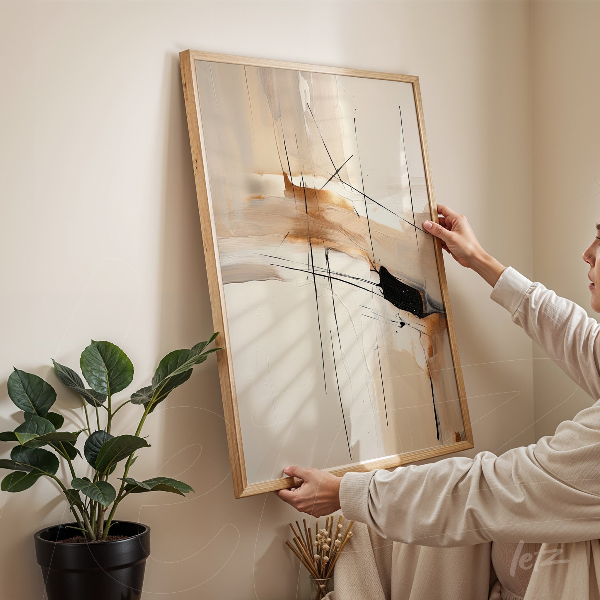 abstract wall art in light wood frame featuring black strokes and neutral tones, displayed next to a potted plant