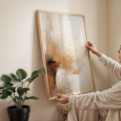 abstract art piece in earthy tones with light wood frame held by a person in a minimalist setting