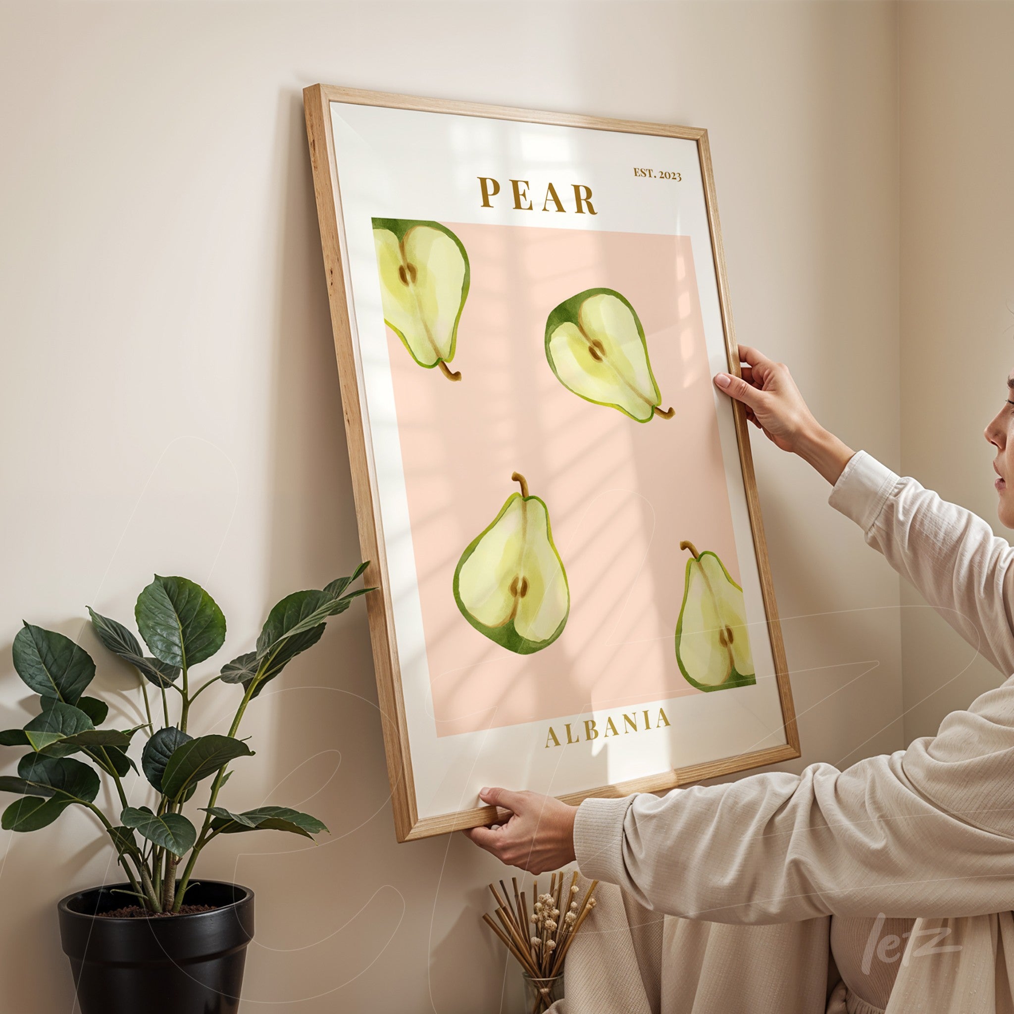 framed wall art featuring pear illustrations on a pink background held by a woman in an indoor setting