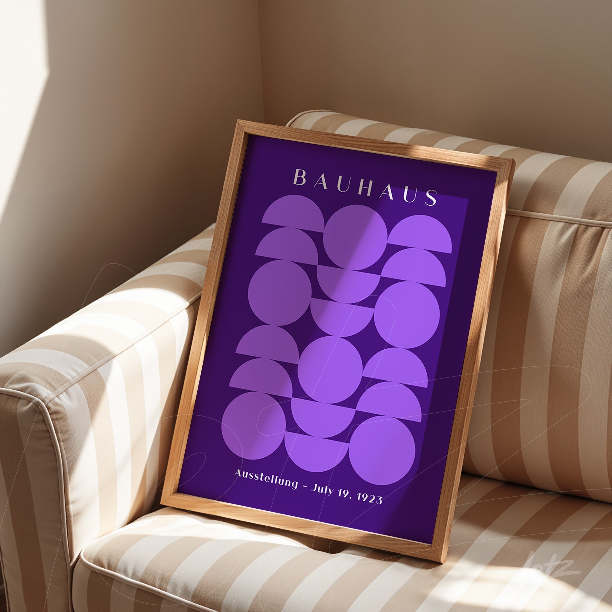 poster with abstract geometric design in purple hues within a light wood frame, displayed on a striped sofa