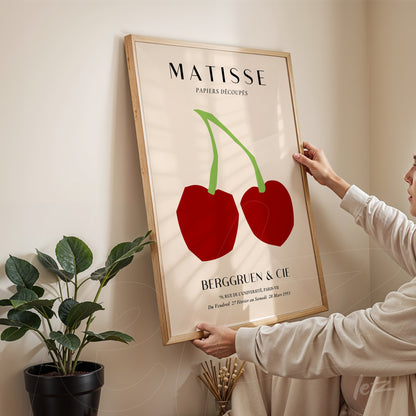 framed art print showcasing two red cherries on a light background with a light wood frame