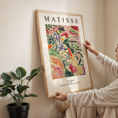 framed artwork by Matisse titled 'La Jalousie' held by a person in a cozy indoor setting with a potted plant in the background