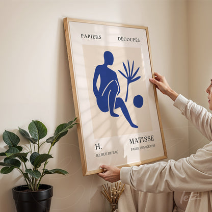 framed art piece featuring a stylized blue figure on a light background with a light wood frame