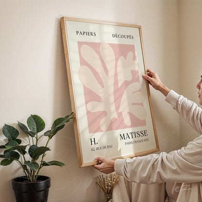framed modern art print featuring pink leaves in pastel tones held by a woman against a beige wall