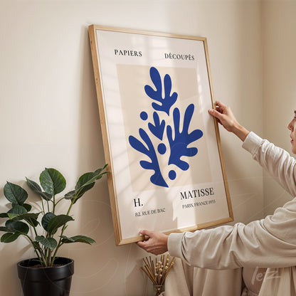 framed modern art featuring abstract blue shapes held by a person in front of a light-colored wall