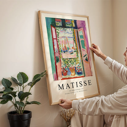 framed artwork by Matisse depicting an open window view of a garden, with light wooden frame
