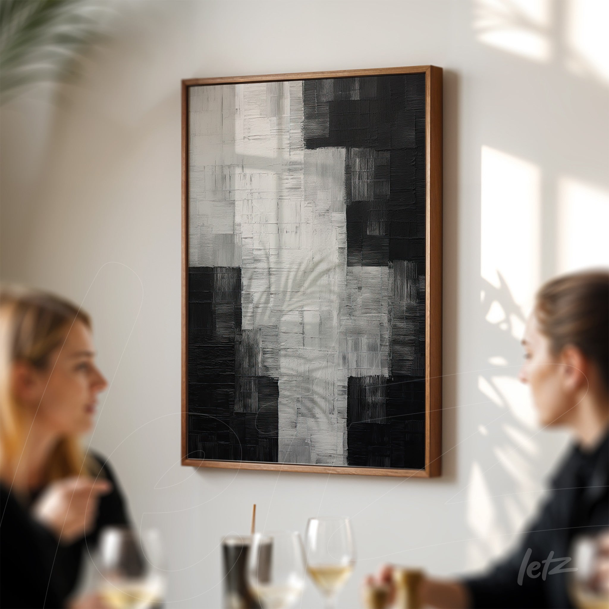 abstract black and white art piece with textured brushstrokes in light wooden frame displayed in dining setting
