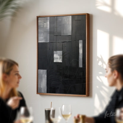 abstract wall art in black and white with textured patterns in a light wood frame displayed on a bright wall in a setting with people