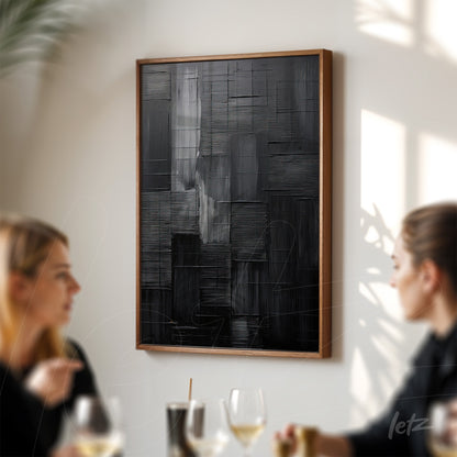 abstract wall art in shades of black with rich texture and light wood frame displayed on a wall illuminated by natural light