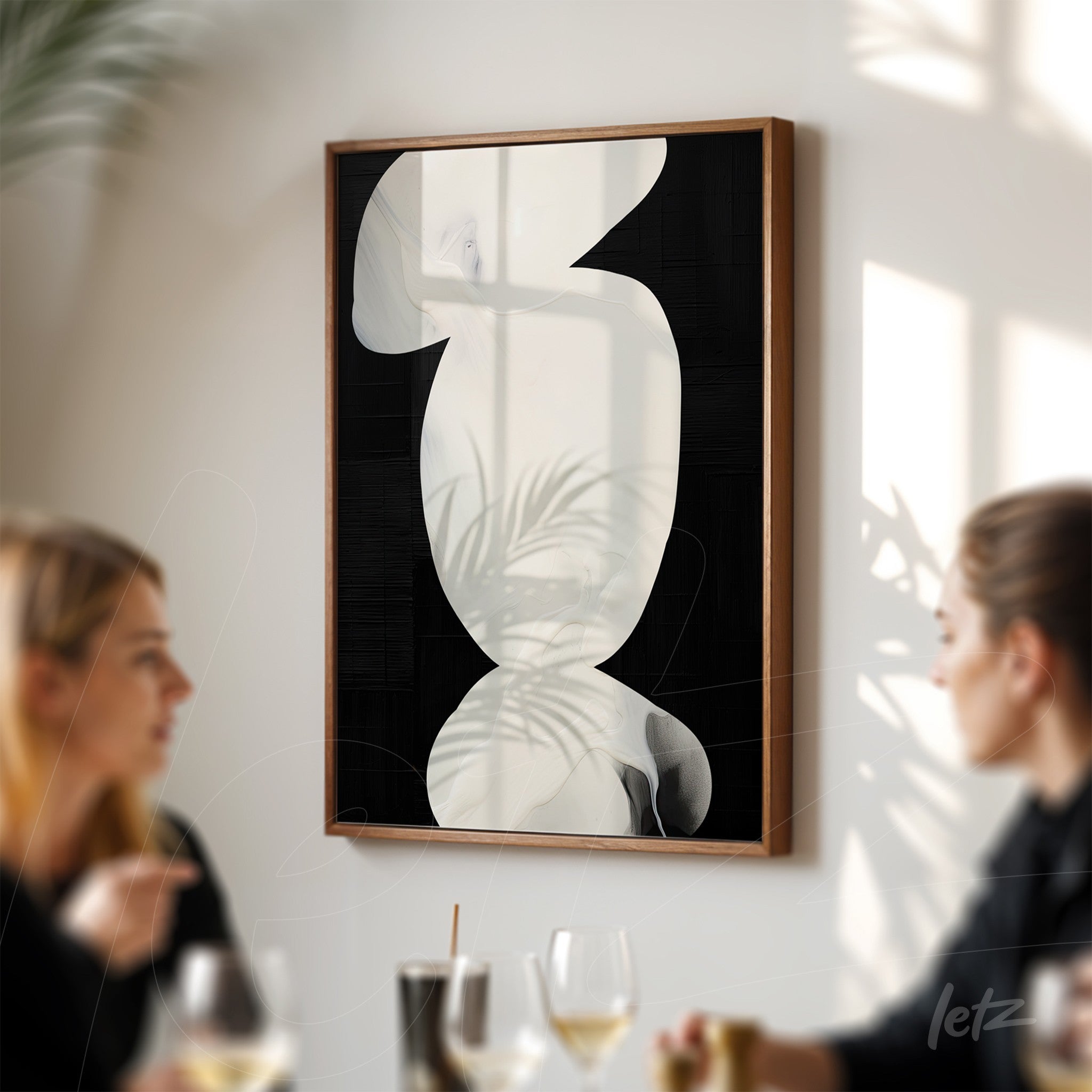 abstract art piece in black and white with a light wood frame displayed on a wall casting leaf shadows