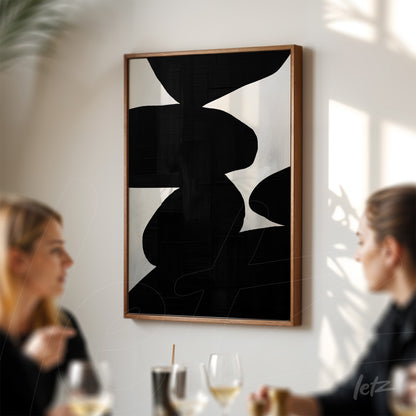 abstract art piece in black and white framed in wood displayed on a light wall with two onlookers in a restaurant setting
