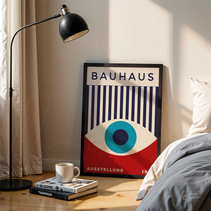 bauhaus poster print in black frame leaning on the floor next to a bed and floor lamp