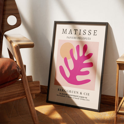 framed modern art piece featuring abstract shapes in pink and orange, leaning against a wooden chair