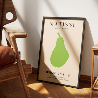 framed wall art featuring an abstract green pear design on a beige background with a minimalist style leaning next to a wooden chair