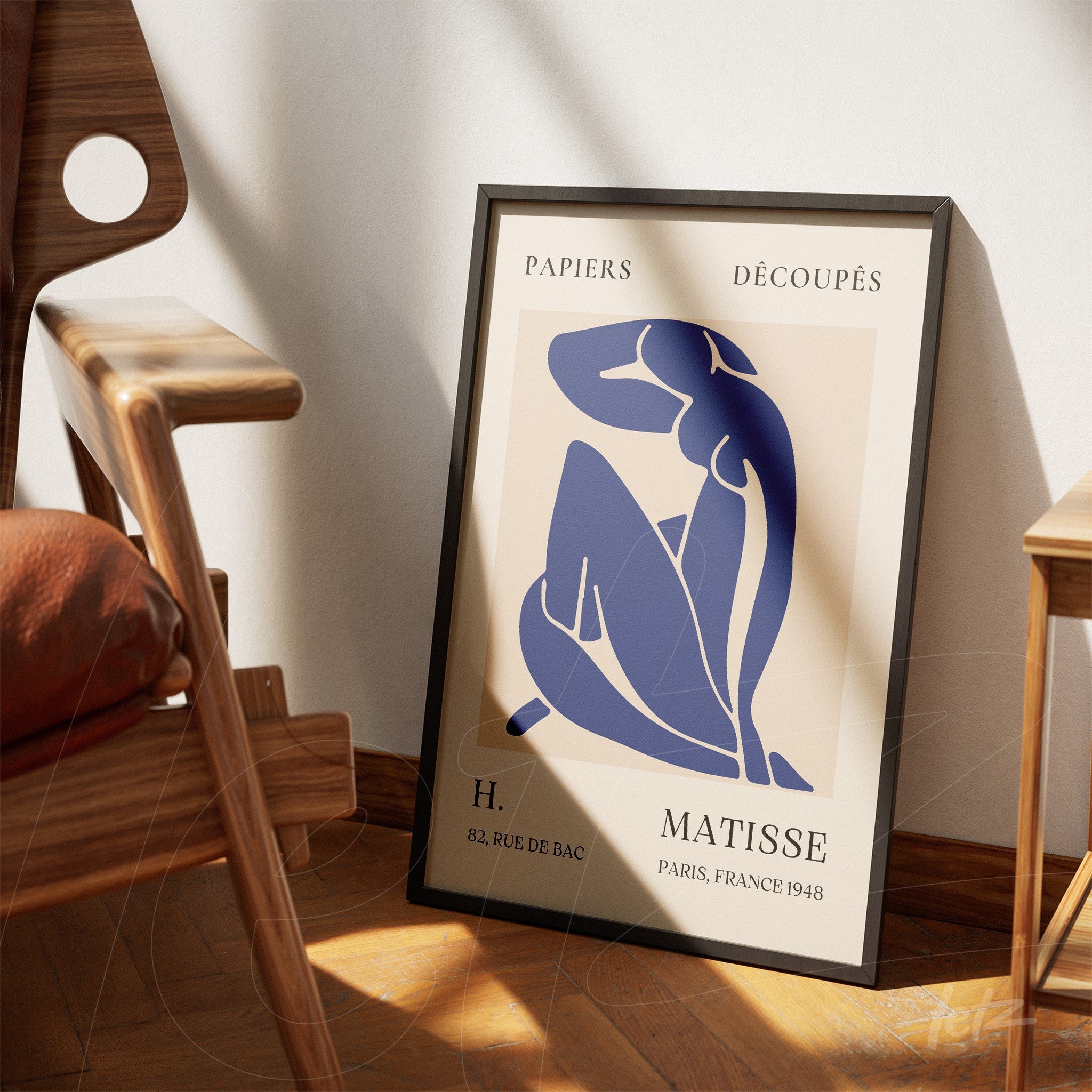 framed artwork in minimalist style featuring a blue female figure, leaning against a light wall next to a modern chair