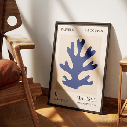 framed modern art print featuring coral shapes in blue, displayed next to a wooden chair