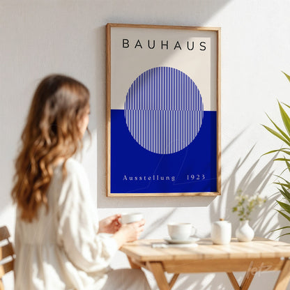 poster with geometric Bauhaus style design featuring a blue circle and stripes on a beige background, displayed in a light wood frame on a white wall