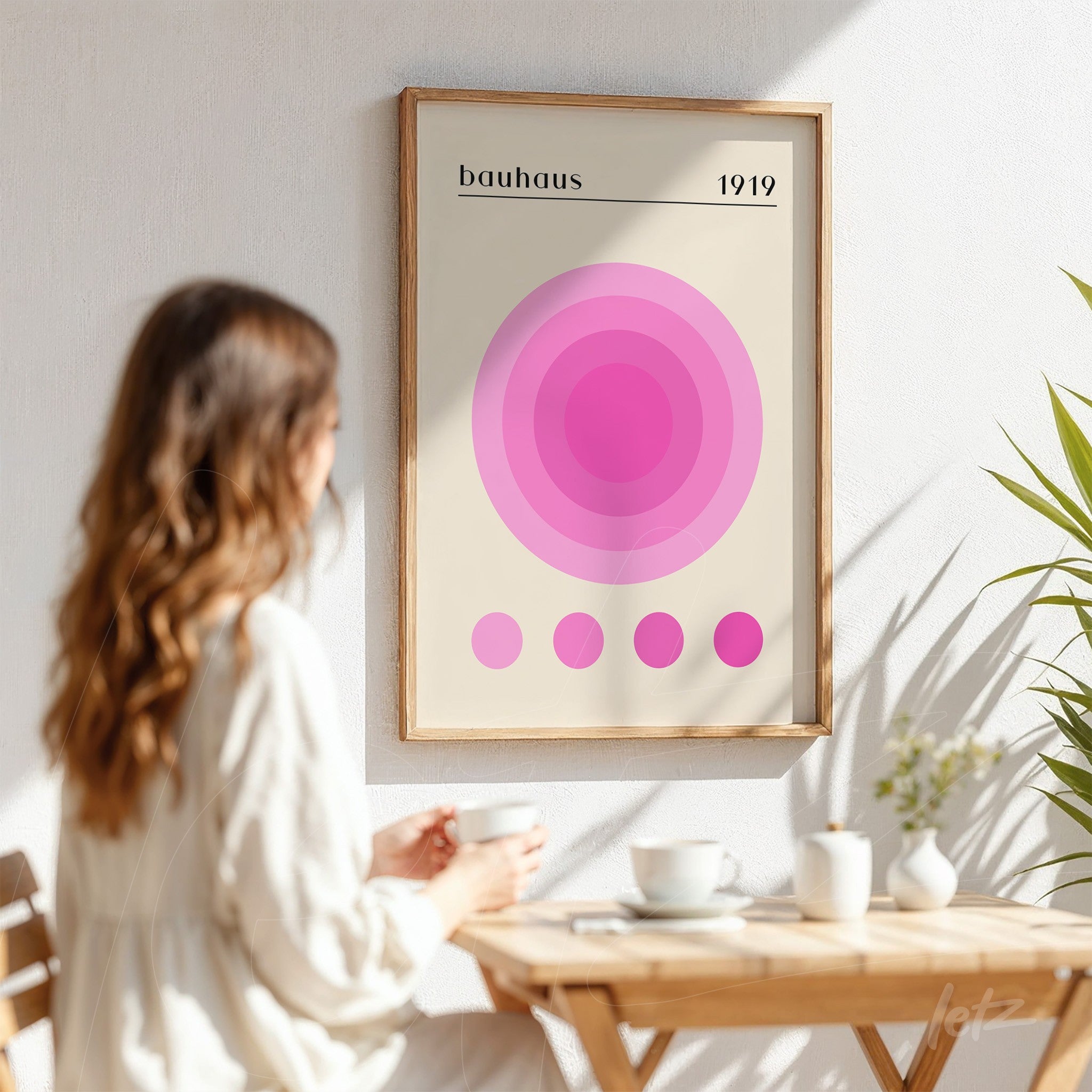 framed wall art with geometric pink circles inspired by Bauhaus style, displayed on a white wall next to a plant