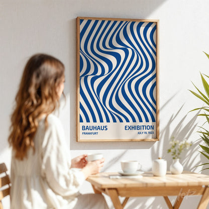 poster featuring abstract wavy blue and white lines in a light wooden frame on a white wall with a woman sitting nearby