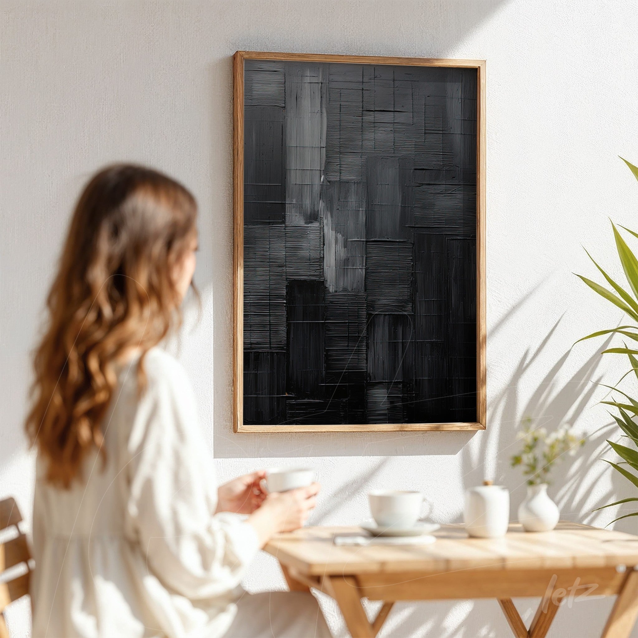 abstract wall art in shades of black with textured design in light wood frame displayed on white wall with natural lighting